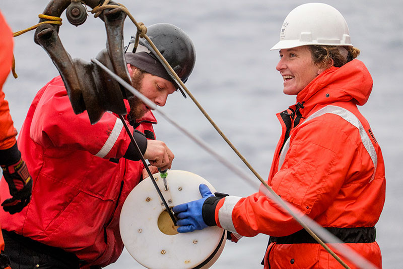 Researchers in high-visibility wet-weather gear on the deck of a research vessel.
